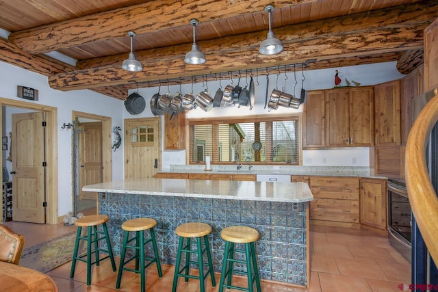 kitchen with wood ceiling, beam ceiling, brown cabinetry, a sink, and a breakfast bar area