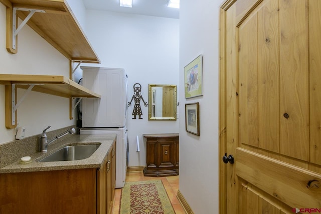laundry room featuring stacked washer and clothes dryer, baseboards, light tile patterned floors, and cabinet space