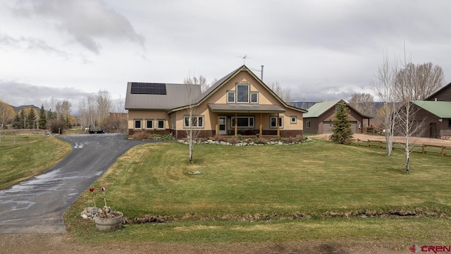 view of front of home with covered porch, solar panels, a front lawn, metal roof, and stucco siding