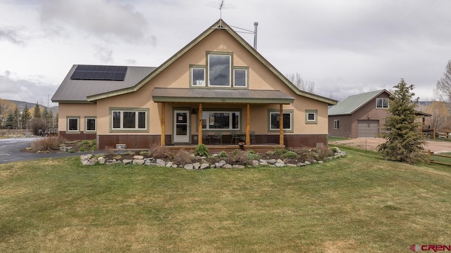 rear view of house with covered porch, stucco siding, solar panels, a lawn, and metal roof
