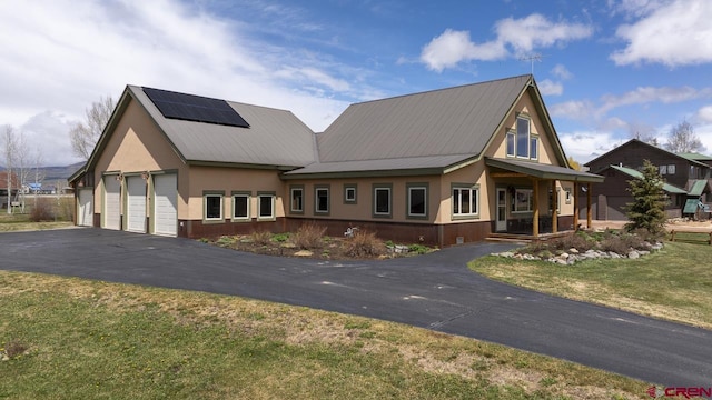 view of front facade with stucco siding, roof mounted solar panels, driveway, a front yard, and metal roof