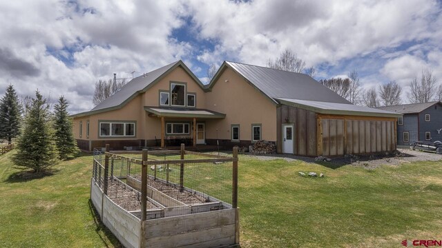 rear view of property with a garden, a yard, metal roof, and stucco siding