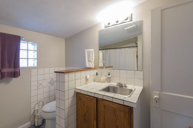 full bathroom featuring toilet, vanity, a textured wall, and tasteful backsplash