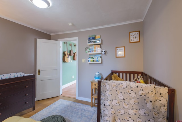 bedroom with light wood finished floors, ornamental molding, a nursery area, and baseboards