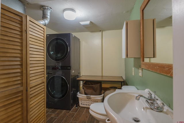 bathroom featuring stacked washer and clothes dryer, a sink, wood finish floors, and toilet