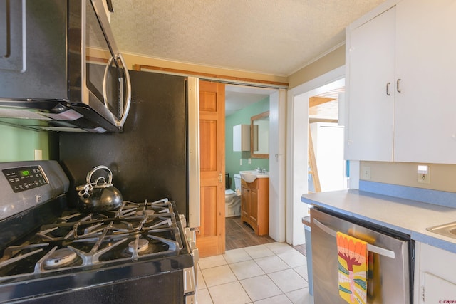 kitchen featuring stainless steel appliances, white cabinetry, light countertops, light tile patterned floors, and a textured ceiling