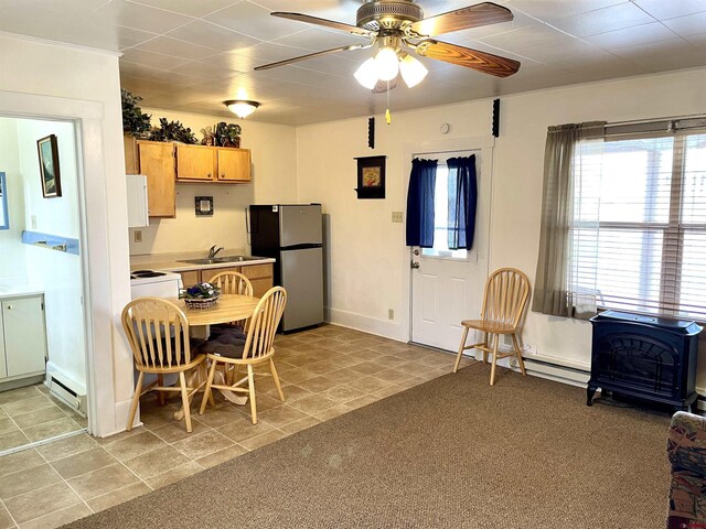 kitchen featuring freestanding refrigerator, a ceiling fan, a sink, a wood stove, and light countertops