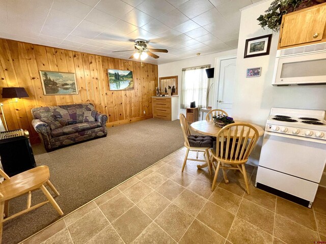 carpeted dining area featuring wooden walls, a ceiling fan, and baseboards