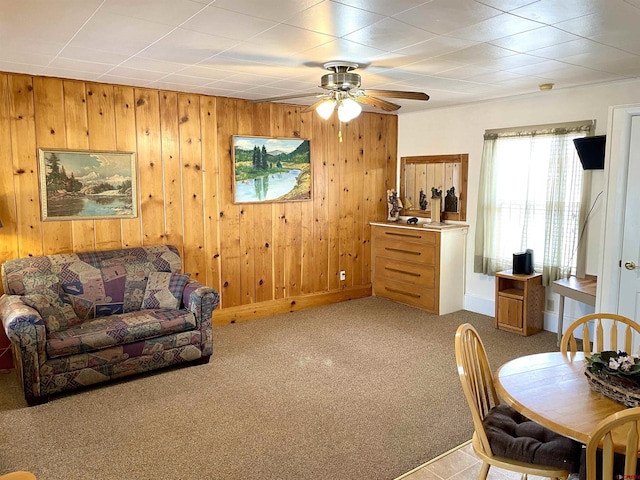 living room with a ceiling fan, carpet flooring, wood walls, and baseboards