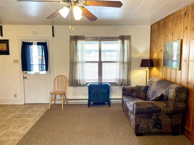 tiled living room featuring plenty of natural light, wooden walls, ceiling fan, baseboard heating, and a wood stove