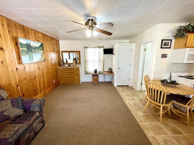 living area with wooden walls, a ceiling fan, and baseboards