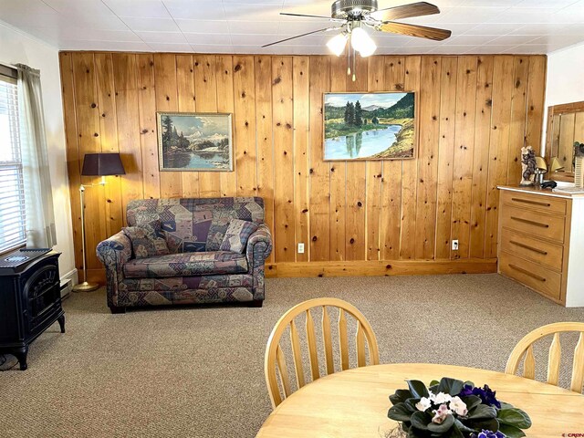 living room featuring a wood stove, wood walls, carpet floors, and a ceiling fan
