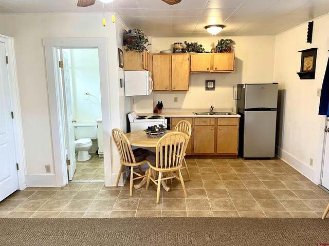 kitchen with white appliances, a sink, light countertops, baseboards, and ceiling fan
