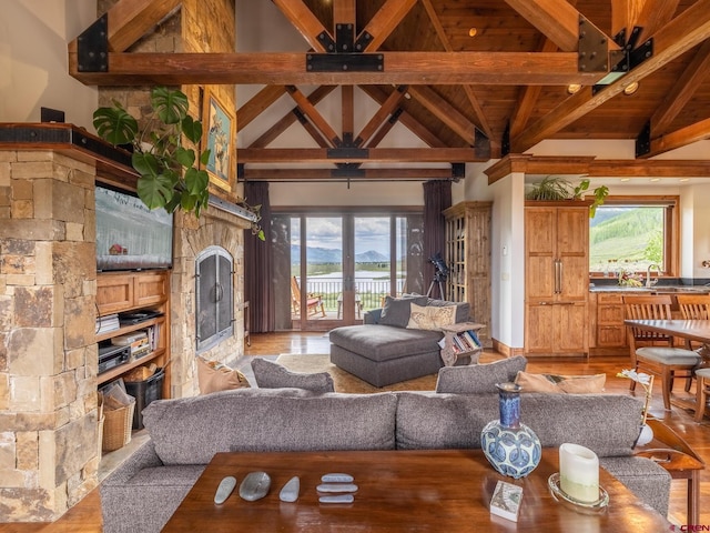living room with a stone fireplace, beam ceiling, light wood-type flooring, plenty of natural light, and wood ceiling