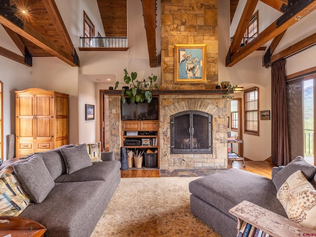living area featuring high vaulted ceiling, beam ceiling, wood finished floors, and a stone fireplace