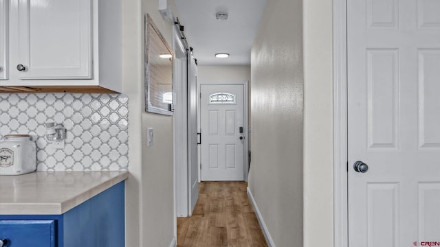 hallway featuring light wood-style floors, baseboards, and a barn door