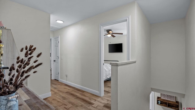 hall featuring light wood-style floors, baseboards, and an upstairs landing