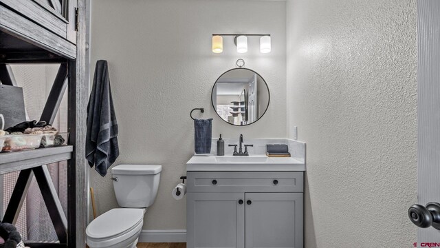 bathroom featuring toilet, vanity, and a textured wall