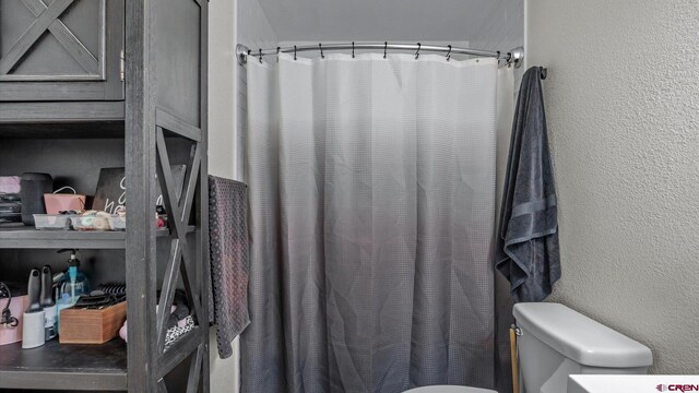 full bathroom with toilet, a textured wall, and curtained shower