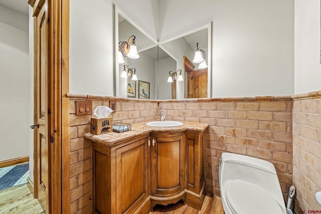 half bath with wood finished floors, wainscoting, toilet, and vanity