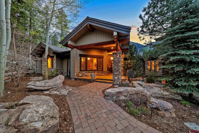 back of house at dusk featuring a porch, stone siding, and board and batten siding