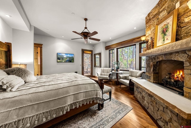 bedroom featuring hardwood / wood-style flooring, a stone fireplace, access to outside, recessed lighting, and ceiling fan