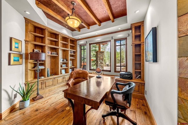 office space with baseboards, beam ceiling, hardwood / wood-style flooring, a raised ceiling, and built in shelves