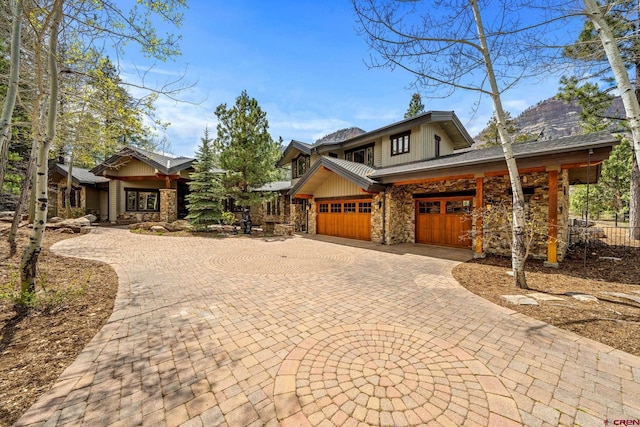 view of front facade with stone siding, curved driveway, board and batten siding, an attached garage, and fence
