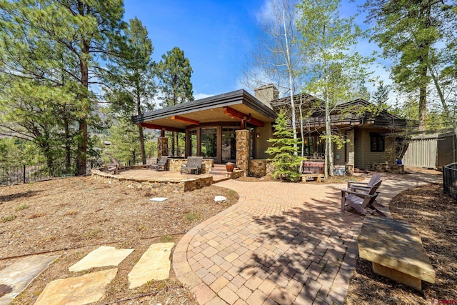 rear view of house with a patio, a chimney, stone siding, and fence