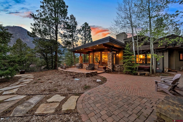 back of property at dusk featuring fence, stone siding, and a patio area