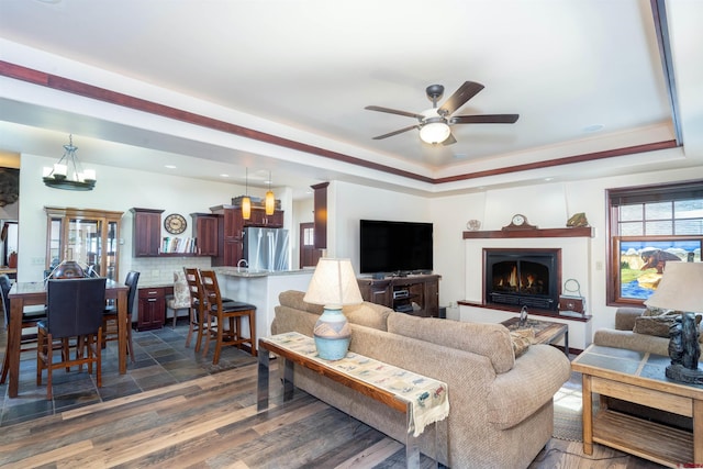 living area with a raised ceiling, a ceiling fan, a lit fireplace, and dark wood-style flooring