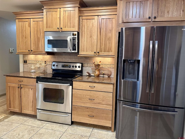 kitchen with stainless steel appliances, tasteful backsplash, dark stone counters, and light tile patterned flooring