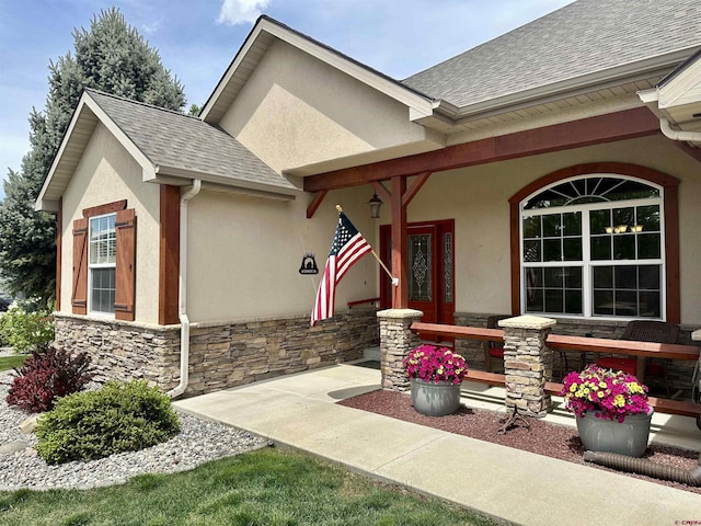 doorway to property featuring stone siding, roof with shingles, stucco siding, and covered porch