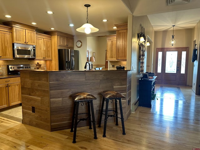 kitchen with stainless steel appliances, dark countertops, a breakfast bar area, decorative backsplash, and baseboard heating