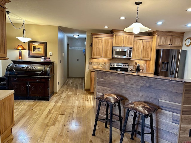 kitchen with appliances with stainless steel finishes, decorative backsplash, light wood-type flooring, a kitchen bar, and decorative light fixtures