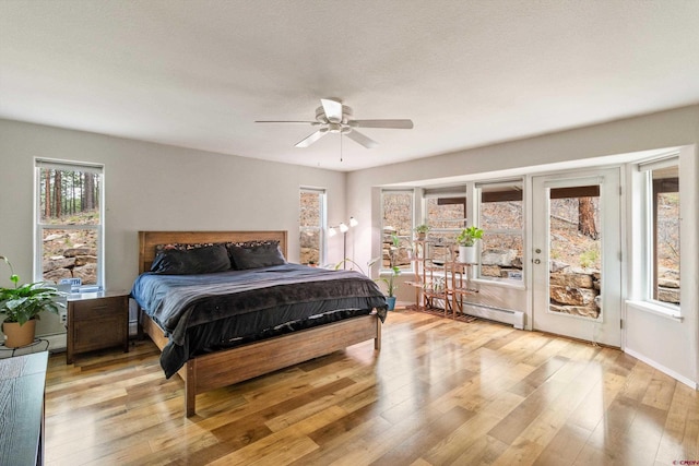 bedroom with access to outside, light wood-type flooring, baseboard heating, and a ceiling fan