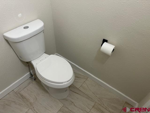 1414 Bluff St, Delta, CO 81416 - bathroom featuring toilet, baseboards, and marble look tile flooring