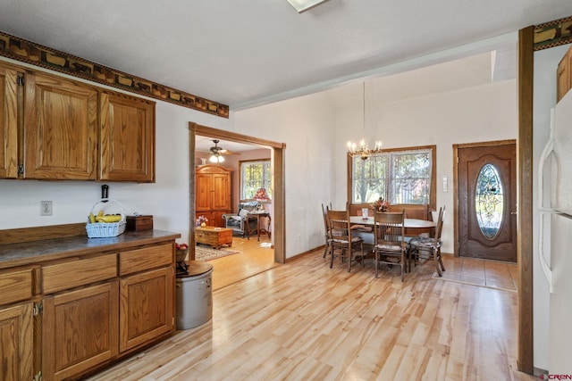 kitchen with brown cabinets, dark countertops, a chandelier, light wood-style floors, and freestanding refrigerator