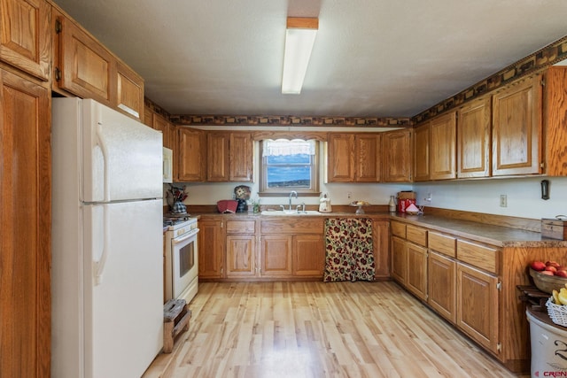 kitchen featuring white appliances, a sink, brown cabinetry, and light wood-style flooring
