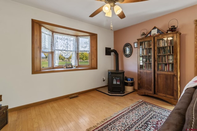 sitting room featuring a wood stove, ceiling fan, baseboards, and wood finished floors