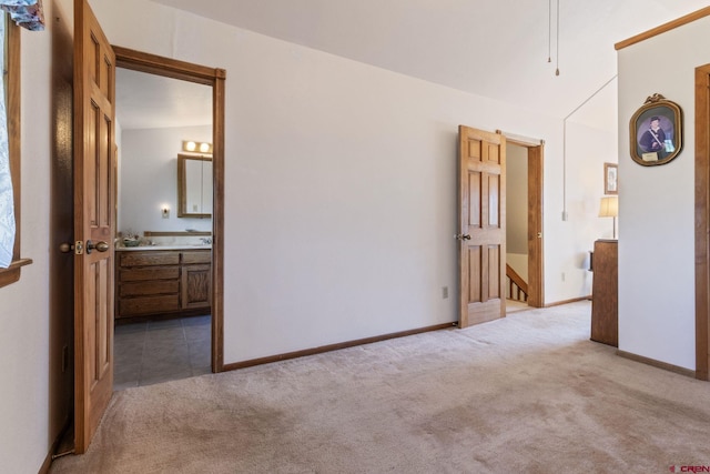 unfurnished bedroom with light colored carpet, ensuite bathroom, and baseboards