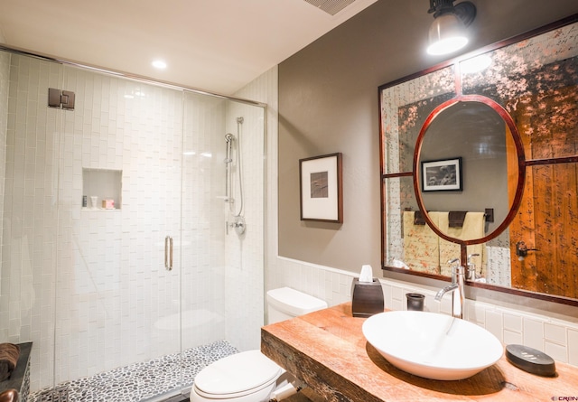 bathroom featuring toilet, a sink, a shower stall, and wainscoting