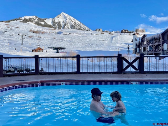 snow covered pool featuring fence, a community pool, and a mountain view