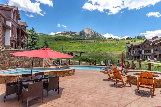 community pool with an outdoor fire pit, a mountain view, a patio, a community hot tub, and fence