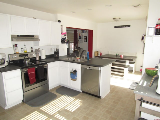 kitchen featuring appliances with stainless steel finishes, a sink, a peninsula, and dark countertops
