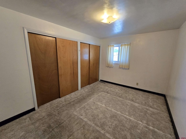 unfurnished bedroom with two closets, carpet, and baseboards