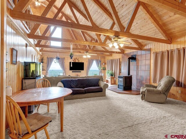 carpeted living area featuring a wood stove, ceiling fan, and wood ceiling