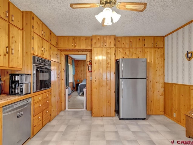 kitchen featuring appliances with stainless steel finishes, wooden walls, ceiling fan, a textured ceiling, and light countertops
