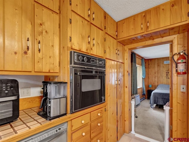 kitchen featuring oven, tile countertops, stainless steel dishwasher, a textured ceiling, and wood walls
