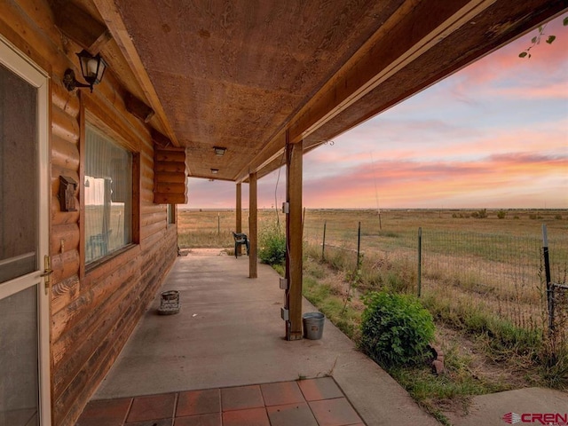patio terrace at dusk featuring fence and a view of rural / pastoral area